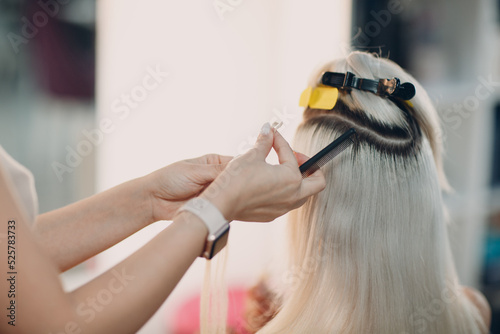 Hairdresser female making hair extensions to young woman with blonde hair in beauty salon. Professional hair extension