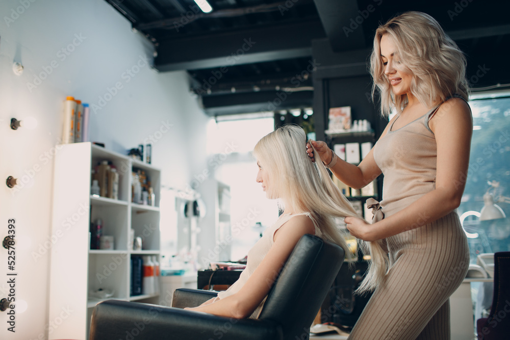Hairdresser female making hair extensions to young woman with blonde hair in beauty salon. Professional hair extension Hairdresser female making hair extensions to young woman with blonde hair in beauty salon. Professional hair extension