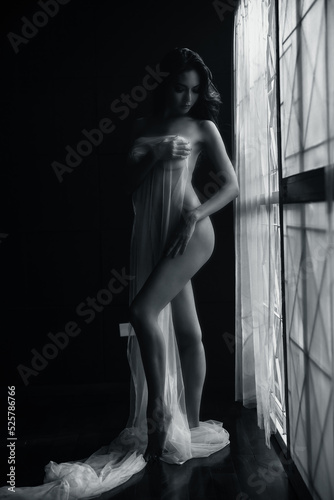 black and white young asian women model standing poses naked by the window light only a thin curtain envelops her and dark background, lady sexy emotion of art