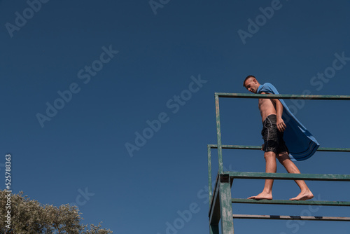 young teen boy near the river having fun with friends at a summer party wearing towel as a superhero scarf ready for a jump looking brave in distance