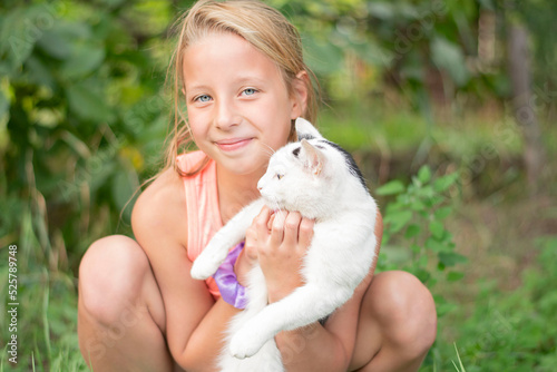 Beautiful caucasian girl holding a white cat in her arms outdoors in summer.