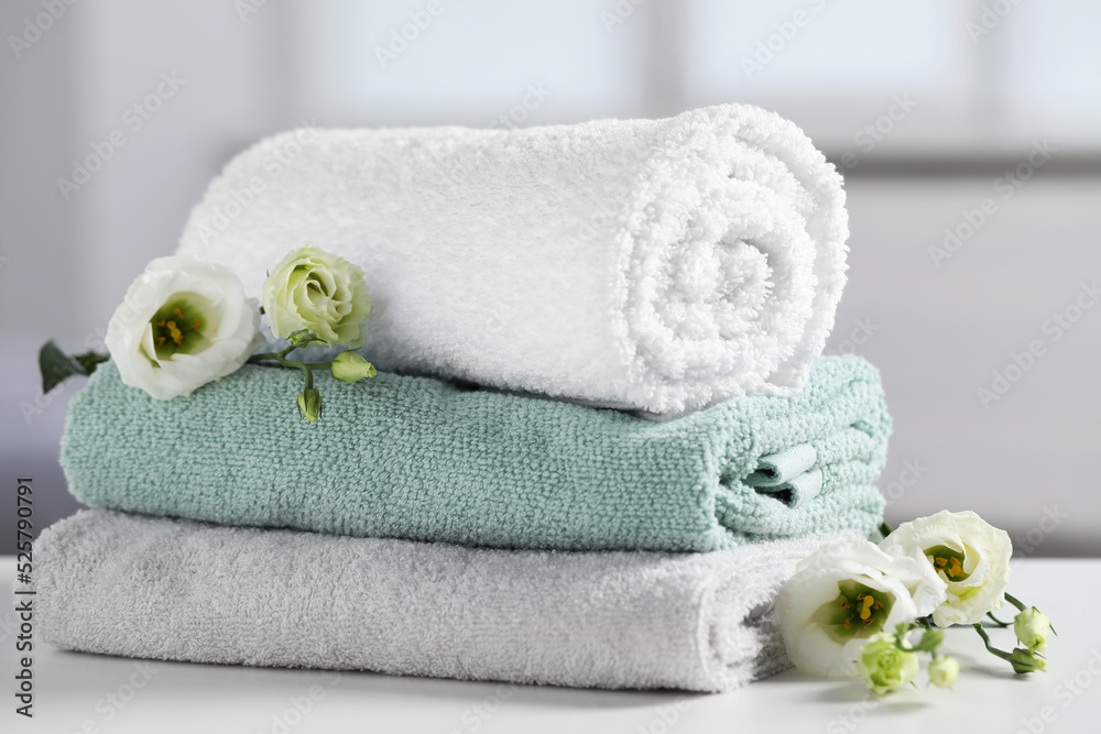 Stack of folded colorful towels with flowers on white table indoors, closeup Stack of folded colorful towels with flowers on white table indoors, closeup