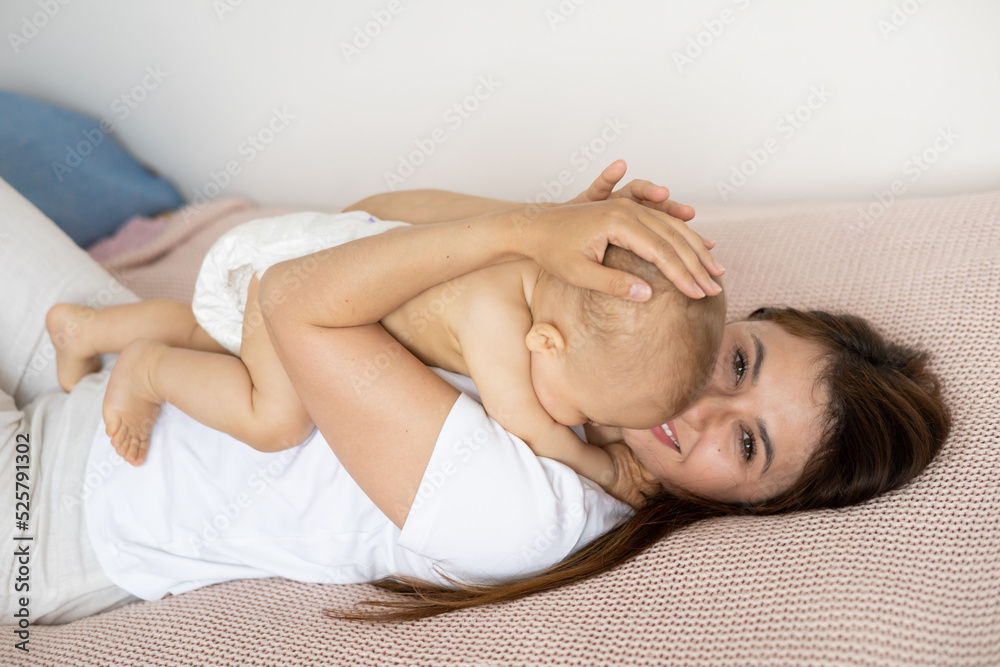 Naklejka premium A beautiful young mother plays and cuddles with her baby in her bedroom on the bed. Love. motherhood Weasel tenderness. Lifestyle