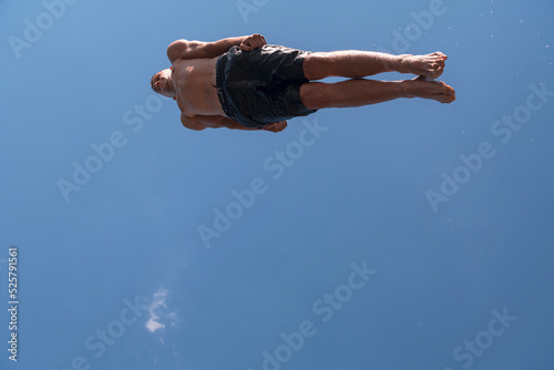 Young teen boy jumping flying and diving in the river. Clear blue sky and trees in distance as a natural background. © .shock