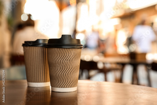 Принти на полотні Cardboard takeaway coffee cups with plastic lids on wooden table in city, space