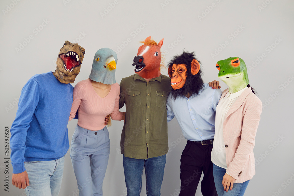Cheerful young people in various original masks in form of animal heads  hugging looking at camera.