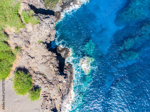 Vue aérienne verticale d'un littoral tropical dans l'océaen Indien avec écume sur l'eau à flanc de falaise, La Réunion © Attraction