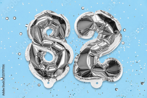 Fototapeta Naklejka Na Ścianę i Meble -  Silver foil balloon number, digit eighty two on a blue background with sequins. Birthday greeting card with inscription 82. Top view. Numerical digit. Celebration event, template.