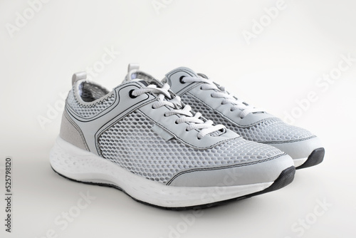 Pair of light-colored summer sneakers with cushioning and ventilation in the form of mesh, standing on a light background, side view. Sporty stylish lifestyle shoes