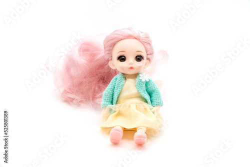 little plastic doll, baby girl. Little blonde doll with blue eyes on white bg. Isolated on white background with shadow reflection. With red shirt and checkered pants.