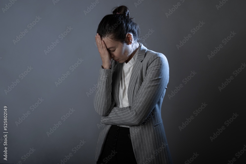 Blood pressure, migraine or headache, a young woman in a business suit standing clutching head, portrait on a gray background Blood pressure, migraine or headache, a young woman in a business suit standing clutching head, portrait on a gray background