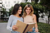 Positive young caucasian girls read abstract before test standing outdoors. Brunettes and blondes wear casual clothes. Education concept