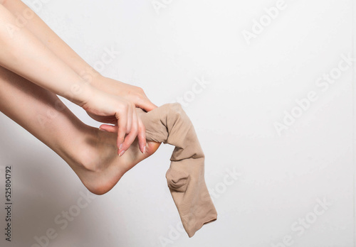 Pregnant girl puts on compression stockings for varicose veins on her legs. White background. Pregnancy and varicose veins, phlebology. photo