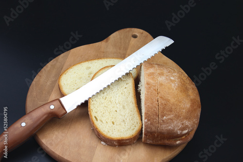 Freshly baked Bread, sliced with a serrated bread knife on a wooden cutting board