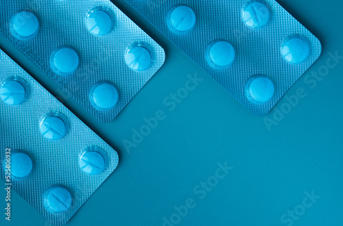 Blisters with blue pills on a blue background. Threeblisters are located in the upper left corner.