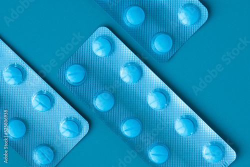 Blisters with blue pills on a blue background. Three blisters arranged diagonally.