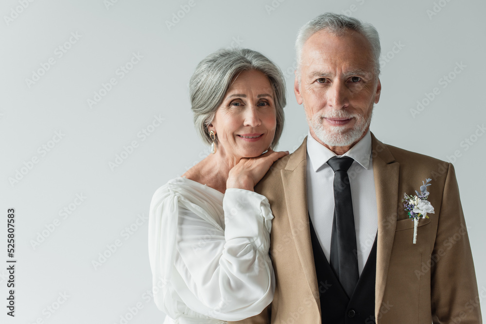 happy middle aged bride in white wedding dress leaning on shoulder of bearded groom isolated on grey happy middle aged bride in white wedding dress leaning on shoulder of bearded groom isolated on grey