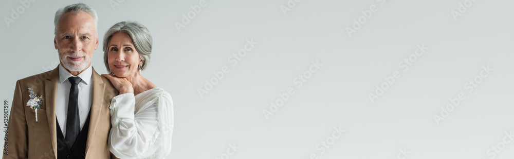 happy middle aged bride in white wedding dress leaning on shoulder of bearded groom isolated on grey, banner happy middle aged bride in white wedding dress leaning on shoulder of bearded groom isolated on grey, banner