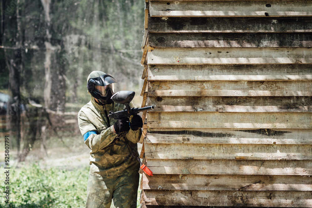 Fototapeta premium Paintball player shooting with marker from behind the wall during the paintball game