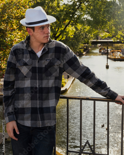 Young hipster wearing a white hat posing in front of a river walk. photo