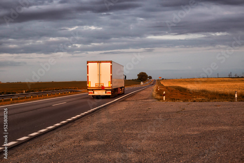 A truck with a trailer transports cargo in the summer against the backdrop of sunset and beautiful evening nature.  photo