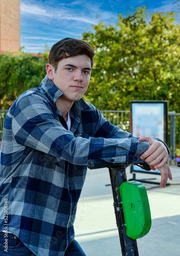 Handsome young man leaning on a scooter with a serious expression.