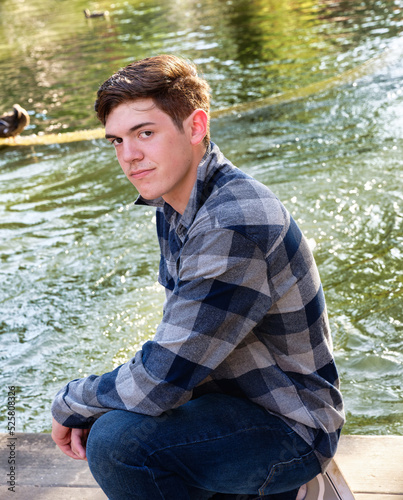 Handsome young man kneeling by a canal with the sun to his back and a confident expression.