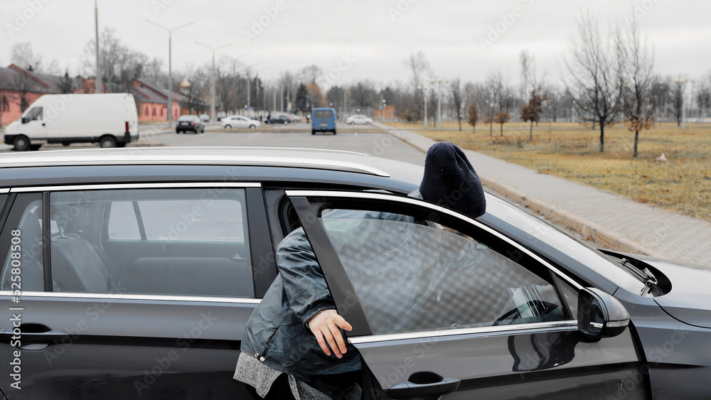 Homeless thief steals purse items money from car in public parking. Auto with unlocked doors open. Property insurance against unlawful theft or crime. Male burglar looks through crack in window. Homeless thief steals purse items money from car in public parking. Auto with unlocked doors open. Property insurance against unlawful theft or crime. Male burglar looks through crack in window.