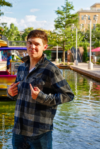 Handsome young man standing by a canal with the sun to his back confidently pointing at himself.