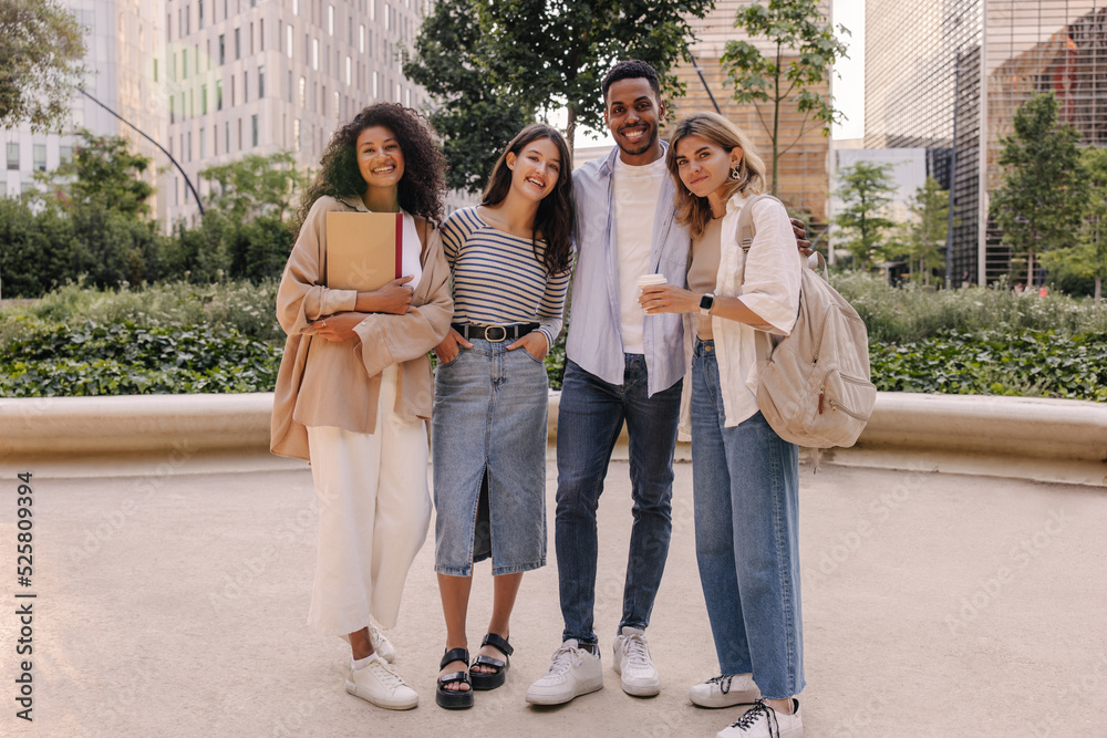 Fototapeta premium In full growth, good young classmates of caucasian, african appearance spend leisure time together on street. Guy and girls wear casual clothes to study. Relax, lifestyle concept