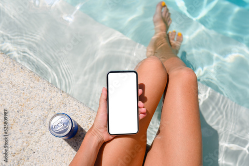 Close-up of a girl by the pool with a smartphone. Top view from above, smartphone with blank white display.