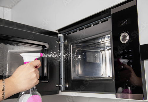 A man sprays a cleaning agent to eliminate unpleasant odors inside a microwave oven, close-up. Cleaning and care of modern household appliances in the kitchen, close-up