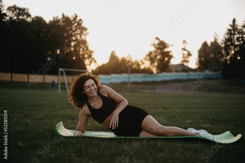 positive young curly woman on a gymnastic mat exercising outdoors. Outdoor yoga classes.
