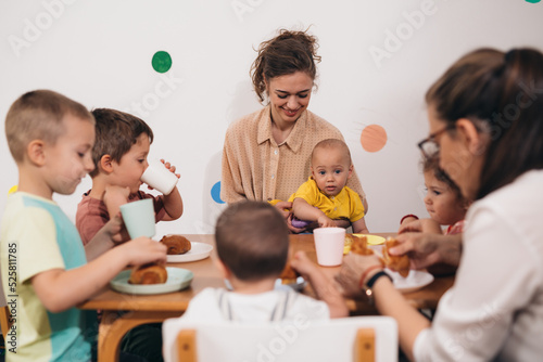 Photos teacher and kids having breakfast in daycare