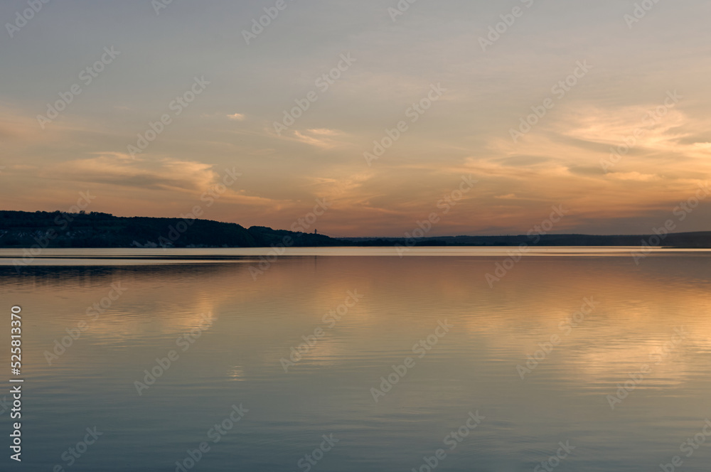 Sunset on a large river, calm water surface, which reflects the sunset sky, the first twilight, serene beautiful landscape