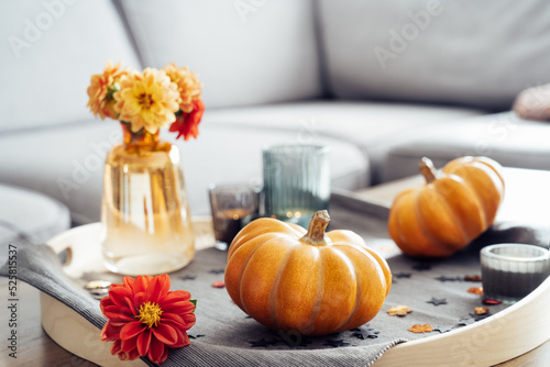 Autumn  fall cozy mood composition for hygge home decor. Small pumpkins  burning candles and fresh dahlia flowers on the tray with gray napkin on the coffee table in the living room. Selective focus