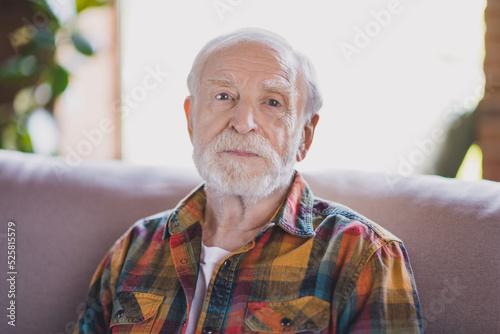 Close up photo of handsome grandpa grey hair serious look camera wear casual checkered shirt sitting cozy sofa indoors home room