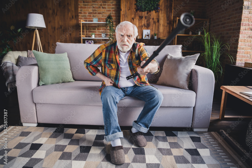 Obraz premium Photo of angry furious retired man dressed plaid shirt sitting couch rising nursery cane indoors apartment