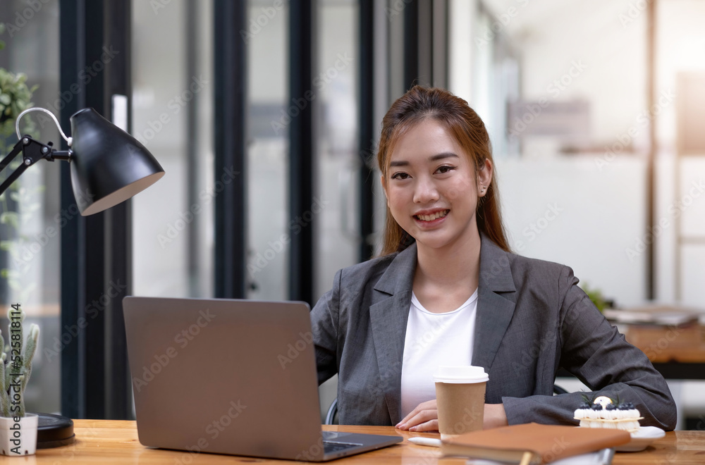 Charming Asian woman working at the office using a laptop Looking at the camera.