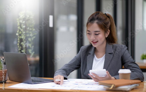 Pretty and charming asian businesswoman sitting happily smiling with laptop computer in the office.