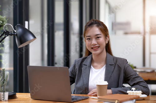 Charming Asian woman working at the office using a laptop Looking at the camera.
