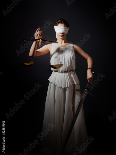 Themis, the goddess of justice blindfolded, with scales and a sword in her hands. A fair trial. Antique goddess, photo on a black background