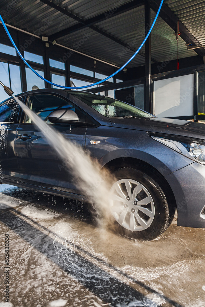 A man washes the wheels on his car at a self-service car wash using a hose with pressurized water