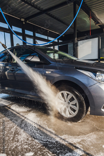 Obraz na płótnie A man washes the wheels on his car at a self-service car wash using a hose with pressurized water w salonie