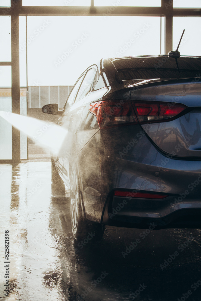 A man washes his car at a self-service car wash using a hose with pressurized water