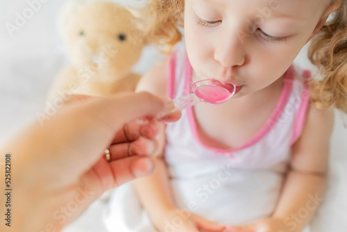 The child drinks syrup from a measuring spoon. Treatment at home.