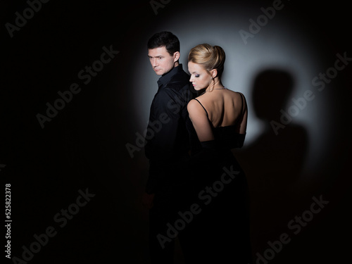 An attractive couple in black. Stylish and elegant young man and woman in the spotlight. Beautiful blonde in a long dress and a guy in a black shirt,