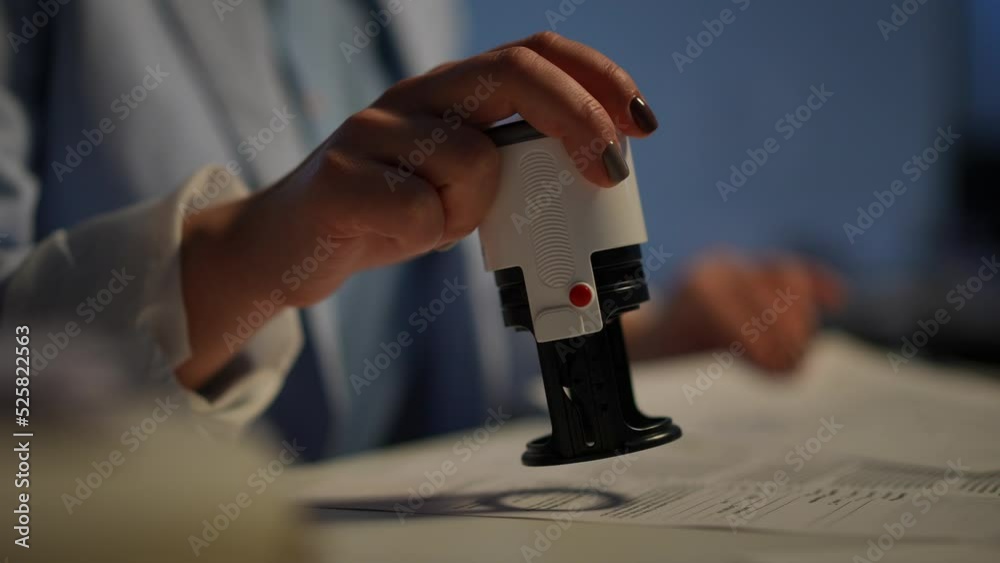 Close-up female hand stamping documents on table in office indoors. Unrecognizable young Caucasian woman working with paperwork. Business and accounting concept
