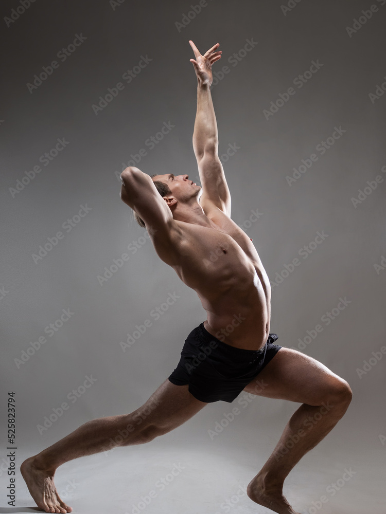 A young muscular man in an expressive pose, throwing his hands up. Beautiful muscles. extraordinary athletic body. Portrait on a gray background