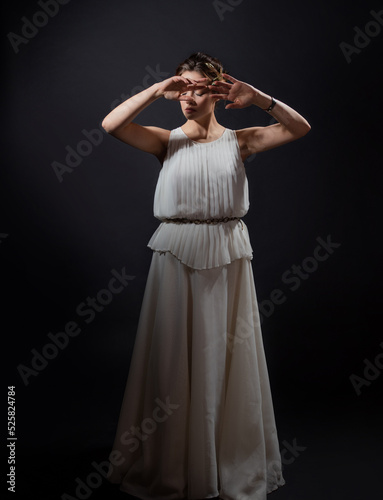 An ancient heroine  a young woman in the image of an ancient Greek goddess or muse. A noble heroine in a white tunic and a laurel wreath  dancing on a black background